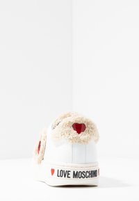 Vit låg sneaker med en fluffig, beige baksida och röda hjärtaccent. Har "LOVE MOSCHINO" i svart på sulan. Slät lädermaterial.
