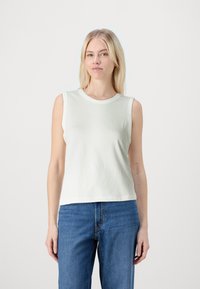 Top sin mangas de algodón verde claro con escote redondo, que presenta una textura suave y un ajuste relajado, combinado con unos vaqueros azul de cintura alta.