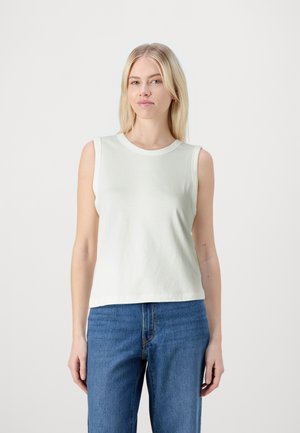 Sleeveless light green cotton top with a round neckline, featuring a soft texture and a relaxed fit, paired with high-waisted blue jeans.