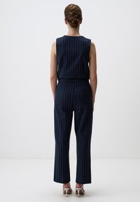 Marine jumpsuit met verticale witte strepen, mouwloos ontwerp, elastische taille, brede broekspijpen en een subtiele textuur in de stof.