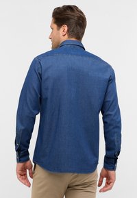 Camicia di jeans blu scuro con maniche lunghe, polsini con bottoni e colletto classico. La texture liscia e la vestibilità regolare esaltano il design.