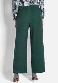 Groene, gestructureerde wijde broek met hoge taille, gecombineerd met grijze hakken. De stof lijkt zacht, wat zorgt voor een ontspannen fit.