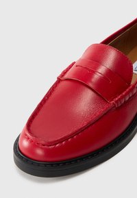 Red leather loafer with a smooth finish, featuring a decorative strap and stitching details, and a black rubber sole for traction.
