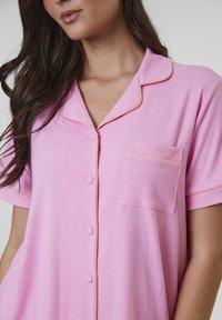 Rosa ribbad pyjamasöverdel med korta ärmar, notchkollare och gula pipingdetaljer. Har en enda bröstficka och knappstängning.