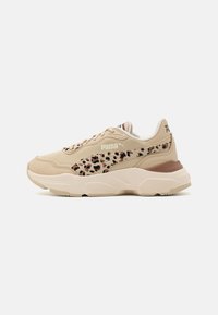 Beige tenisky Puma s leopardím potiskem na bočním pruhu, robustní bílou podrážkou a šněrovacím designem, zobrazené z vnější strany na bílém pozadí.