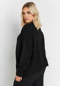 Svart oversized stickad tröja med texturerad tyg, sänkt axlar och långa ärmar. Har en lös passform, perfekt för lager-på-lager-styling.