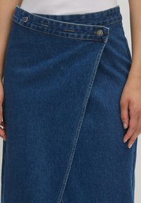 Denim rok met een wikkelontwerp, donkerblauwe kleur, zilveren knoopaccenten en een soepele textuur met zichtbare stiksels.