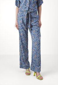 Sininen kukkakuosiset pyjamapaita, jossa on lyhyet hihat ja leveät housut, joissa on solmittava naru. Pehmeä kangas, jossa on paisley-kuvioita ja eloisia värejä.