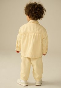 Veste et pantalon à rayures jaunes et blanches en tissu doux, avec une coupe décontractée et une fermeture à bouton-pression, associés à des baskets blanches.