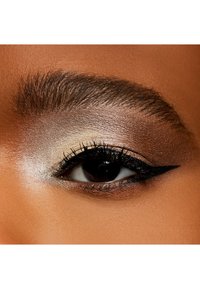 Nærbillede af et øje med lagdelt øjenskygge i beige, guld og brune nuancer, defineret sort eyeliner og tykke, buede vipper.