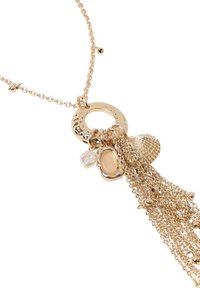 Collana in tono oro con un pendente circolare testurizzato, molteplici catene pendenti e vari ciondoli, tra cui una conchiglia e una perla.