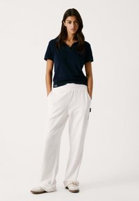 Jūras zilas krāsas polo krekls ar apkakli, kombinēts ar baltām elastīgā jostasvietā sporta biksēm. Baltas kedas ar beigu zoli. Vienkāršs dizains, brīvs piegriezums.