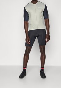 Jersey de ciclismo de manga corta en verde menta claro con mangas azul oscuro, cierre frontal de cremallera, combinado con pantalones cortos acolchados negros y zapatos de ciclismo negros.