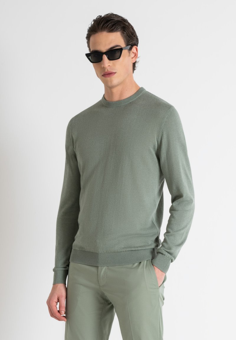Maglione lavorato a maglia verde chiaro con maniche lunghe, scollo a girocollo e polsini a costine, abbinato a pantaloni verdi chiari coordinati.