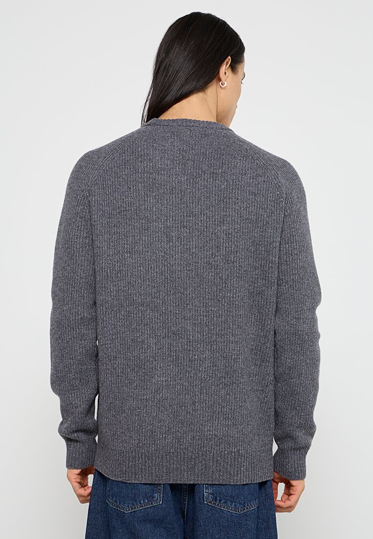 Maglione grigio lavorato a maglia con texture a coste, scollatura a girocollo e maniche lunghe. Nessun marchio o motivo visibile. Vestibilità ampia alla vita.