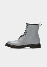 Πλάγια όψη ενός γκρι μποτάκι αστραγάλου με κορδόνια, μαύρη σόλα και κίτρινη ραφή σε λευκό φόντο.