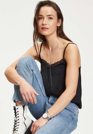 Camisole en soie noire avec dentelle, assortie à un jean déchiré bleu clair, des bottines lacées blanches et des bijoux en argent.