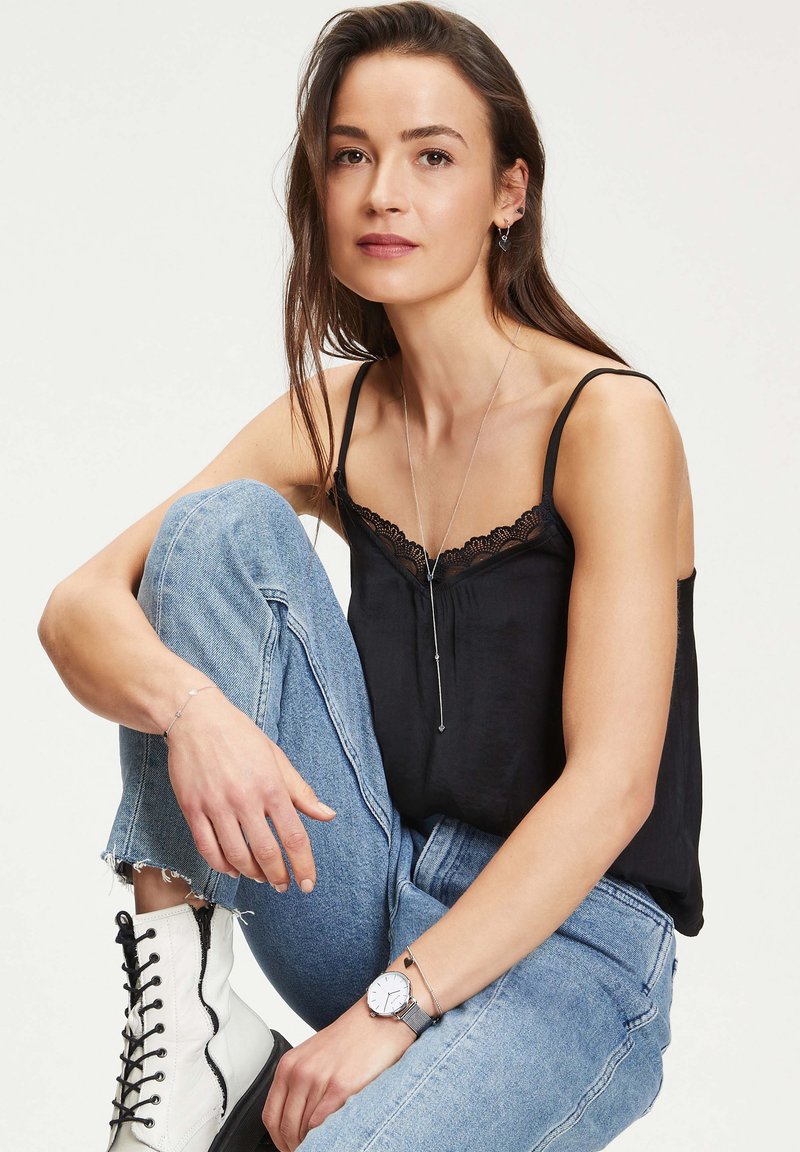 Camisole en soie noire avec dentelle, assortie à un jean déchiré bleu clair, des bottines lacées blanches et des bijoux en argent.