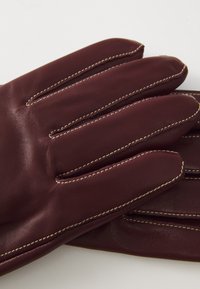 Guantes de cuero burdeos con una textura suave, que presentan una costura cuidada a lo largo de las costuras de los dedos y un diseño clásico.