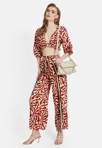 Conjunto de dos piezas en rojo y crema con un top corto de escote en V profundo y pantalones de pierna ancha, complementado con un bolso neutro.