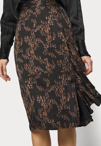 Jupe noire avec un motif abstrait dans des tons orange et violet, avec une texture lisse et élégante, et un détail de pli sur le côté.