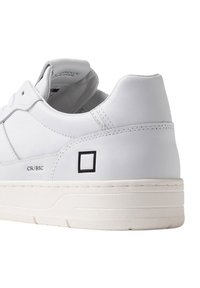 Hvide lædersneakers med en tyk hvid sål, subtile syninger og et sort firkantet accent ved hælen. Rent, minimalistisk design.