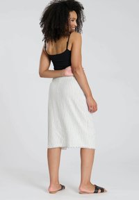 Lichtgewicht, knielange rok in het wit met verticale grijze strepen. Afgewerkte zoom en een zachte textuur. Gedeeltelijk gedragen met een zwart tanktop en zwarte slidesandalen.