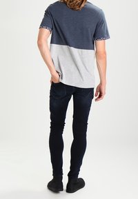 T-paita, jossa on tummansininen yläosa ja harmaa alaosa, lyhyet hihat kuvioiduilla resoreilla. Yhdistetty tummiin slim fit -farkkuihin ja mustiin kenkiin.