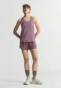 Μωβ αμάνικη μπλούζα και αντίστοιχα σορτς, και τα δύο με ελαφρύ, υφασμάτινο φινίρισμα. Λαδί πράσινες κάλτσες και λευκά αθλητικά παπούτσια ολοκληρώνουν την εμφάνιση.