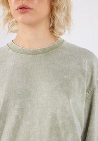 Lysegrønn oversized t-skjorte laget av mykt stoff, med ribbestrikket rund hals og subtil teksturert overflate.