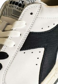 Sneaker in pelle bianca con un accento in pelle nera, punta rotonda, dettagli perforati e lacci bianchi. Logo Diadora sulla linguetta.