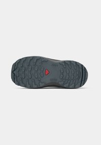 Schwarze Wanderschuhsohle mit einem robusten, strukturierten Design, tiefen Profilnoppen und einem roten Akzentdreieck in der Mitte.