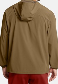 Veste à capuche légère et marron avec une texture lisse, des poignets élastiques et une coupe décontractée. Pas de logos visibles ni de motifs distincts.