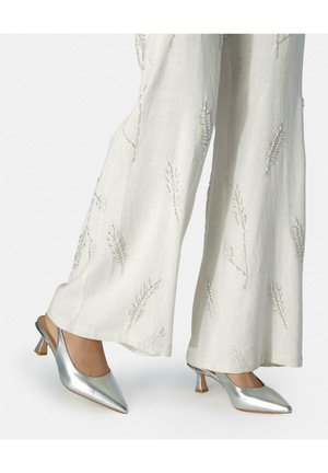 Zapatos slingback plateados de tacón bajo usados con pantalones blancos de pierna ancha bordados con delicados patrones de hojas.