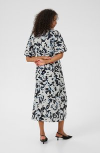 Kukkakuosiset midi-mekko vaaleanharmaana, jossa on puffihihat, mustia ja sinisiä kuvioita sekä suora siluetti. Mustat slingback-korkokengät.