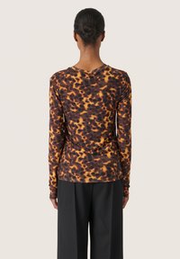 Langärmliges Oberteil mit einem braun-orangefarbenen Leopardenmuster, Rundhalsausschnitt und figurnaher Passform, kombiniert mit schwarzen Hosen.