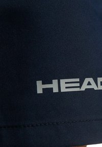 Pantaloncini in tessuto blu navy con una texture liscia che presentano un prominente logo bianco "HEAD" sull'orlo. Dettaglio di cuciture pulite visibile.