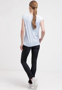 Ljusblå kortärmad t-shirt med avslappnad passform, kombinerad med svarta skinny jeans och silverfärgade sneakers, sedd bakifrån.