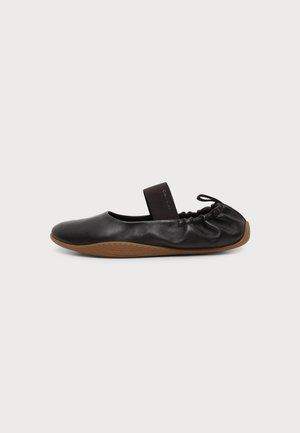 Chaussure plate en cuir noir souple avec semelle marron, sangle élastique sur le cou-de-pied et détail froncé au talon avec petit nœud.