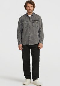 Dark gray denim shirt with two chest pockets, button front, and long sleeves. Paired with black pants and white sneakers.