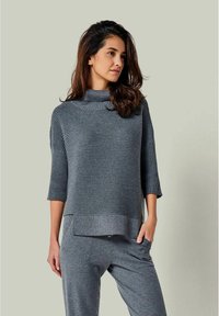 Grauer gerippten Strickpullover mit hohem Kragen, Dreiviertelärmeln und geradem Saum. Weicher Stoff, kombiniert mit grauen Loungehosen.