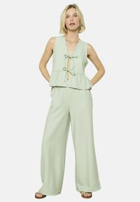 Mint zelena kombinezon z volanom, V-izrezom in detajlom z vezanjem spredaj; ima široke hlače z subtilnim navpičnim črtastim vzorcem.