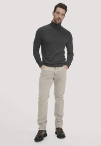 Dunkelgrauer Rollkragenpullover, taillierte Passform, kombiniert mit hellbeigen Hosen. Braune und schwarze Schnürstiefel mit strukturierten Akzenten.