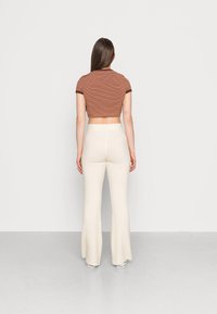 Top cropped listrado em tons de castanho e laranja, combinado com calças flared em creme com textura canelada. Design ajustado, textura suave e detalhe de cós largo.