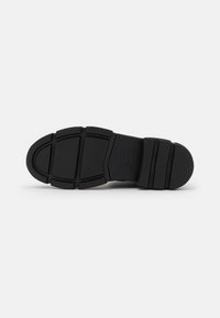 Suola di scarpa in gomma nera con una superficie testurizzata, motivo di battistrada segmentato e tallone rinforzato. Design flessibile per trazione e durata.