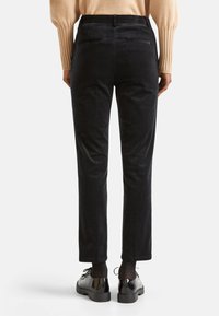 Pantalons en velours côtelé noirs avec une coupe slim, dotés de deux poches arrière, d'une taille mi-haute et d'une texture subtile. Associés à des chaussures noires brillantes.
