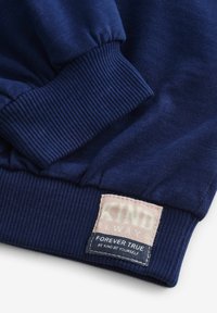 Sweatshirt bleu marine avec des poignets côtelés. Présente une étiquette tissée de couleur rose clair, indiquant "FOREVER TRUE" et "BE KIND. BE YOURSELF."