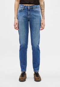 Jeans din denim albastru cu o croială clasică, având cinci buzunare, închidere cu nasture și ușoară decolorare. Asortați cu adidași cu imprimeu de leopard.