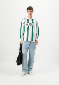 Pitkähihainen paita, jossa on vihreät ja valkoiset pystysuorat raidat, mustalla "F.C.HOUSE" -logolla. Asusteena vaaleansiniset leveät farkut ja valkoiset lenkkarit.