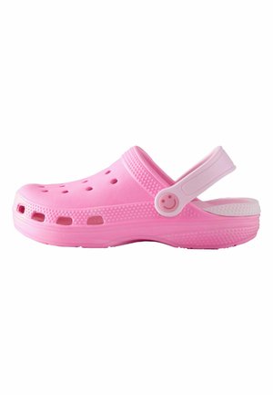Pinkfarbener Kunststoff-Clog mit großen Belüftungslöchern, einer weißen Sohle und einem Riemen mit Schnalle, der an der Seite ein Smiley-Gesicht zeigt.